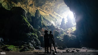 a couple standing inside a Bat Cave in Vietnam, as light enters the cave
