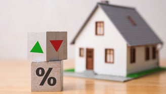 blocks with green and red arrows for interest rates beside tiny house