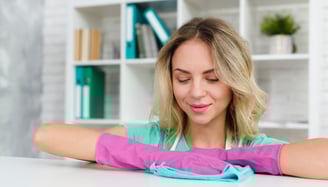 a woman in a green shirt and pink gloves cleaning the desk
