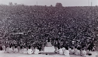 Swami Satchidananda on stage in front of a huge crowd as he opens the Woodstock Festival in 1969