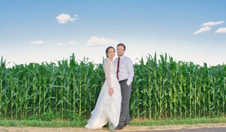 a bride and groom standing in front of a corn field
