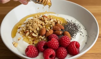 A bowl of Greek yogurt topped with honey, nuts, chia seeds, and fresh raspberries.