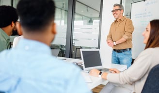 a man in a brown shirt is standing in front of a group of people in a behavioural design workshop