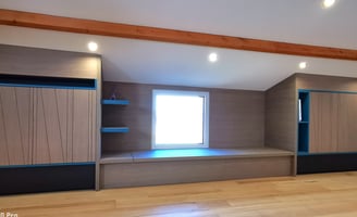 Aménagement sous combles en bois grisé et niches déco bleues. Banc avec rangement, portes usinées.