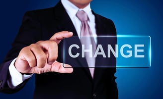 A businessman in a suit and tie holds up a rectangular piece of glass with the word "Change" written on it, face unseen.