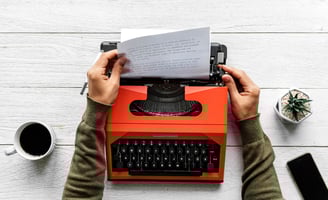 A writer typing on a typewriter, with a focus on the writing process and content creation.