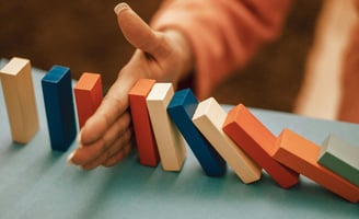 a women's hand stopping dominos from falling