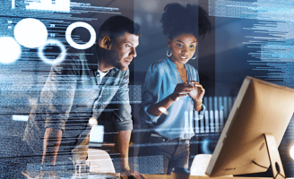 A male and female leader look at a computer monitor as holographic coding and scripts float around them.