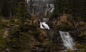 Bride and groom standing on a waterfall in Banff National Park