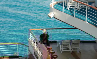 Passageiro em cadeira de rodas na varanda do navio, admirando a vista durante a navegação.