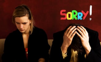 A womand and a man sitting on a couch with a sign that says sorry