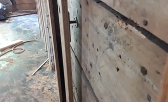 Wall reinforcement in progress with plywood panels and anchor bolts during interior renovation of an older home