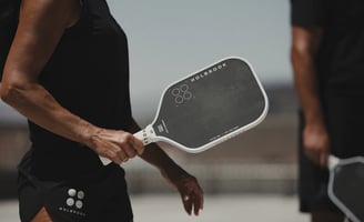 Close-up of athlete holding a black Holbrook pickleball paddle during outdoor match.
