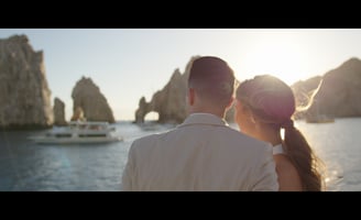 A couple of lovers watching the iconic Cabo San Lucas arch from a boat, with golden light