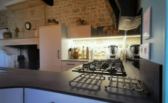 Cuisine beige avec plan de travail pierre. Ilot central, plaque de cuisson gaz. Mur en pierre.