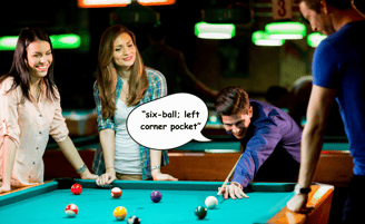 A group of friends smiling and playing a game of pool