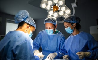 Three surgeons in blue scrubs and masks are focused on operation in operating room.