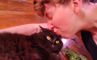 Cassie is lying on the floor kissing their sister's black cat with catnip on the floor