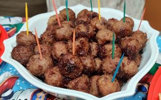 A bowl of crockpot meatballs with colorful toothpicks sticking out on a Christmas tablecloth