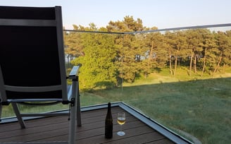 Stuhl mit Blickrichtung Meer steht auf dem Balkon, daneben ein Glas und eine Flasche Wein