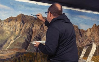 Martin Osner painting a large mountain landscape on canvas using acrylics and a palette, painting on a ladder