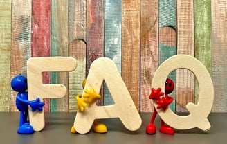 3 toy figures, each holding one letter of FAQ. Standing in front of painted wooden boards