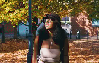 Young college black woman smiling and birdwatching underneath golden yellow autumn trees.