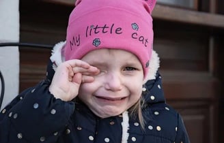 Enfant qui pleure avec bonnet rose (avec inscription My little cat) et doigts main droite sur l'oeil
