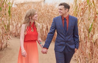 a man and woman holding hands and walking through a corn maze