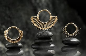 Three gold septum rings with black gemstone accents, displayed on stacked black stones against a dark background for e-com