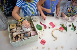 Children's hands reaching into a bin of stamps and supplies.