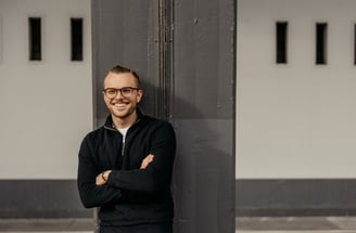 a man with glasses and a black jacket standing in front of a building
