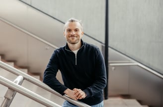 a man in a black jacket and jeans standing on a stair case