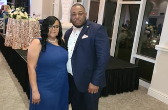 Pastor posing with his wife in suit and dress in ballroom