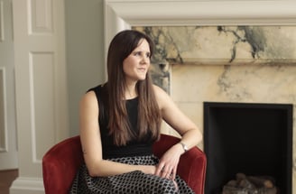 Photo of Anna Joyce expert insomnia therapist sitting in chair by marble fireplace wearing a dress