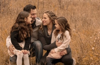 a family photo of three sitting on a field of tall grass