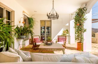 Terrace with wooden seating, pink cushions, plants, and a chandelier in rustic style.