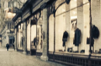 Softly blurred London street scene with a pedestrian walking past illuminated shop windows displaying coats and reflections