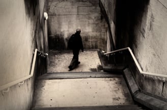 Photograph of a lone man dressed in black walking down a dimly lit subway staircase in London, captured in the early morning 