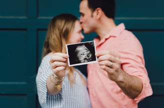 a pregnant woman and her husband kissing in front of a blue wall