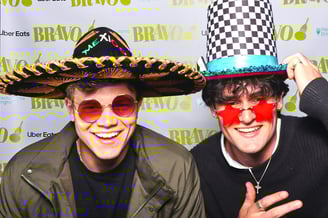 Two young men smile for a photo in Get The Picture photo booth wearing fun hats and glasses at awards party