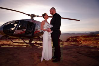 a bride and groom standing in front of a helicopter