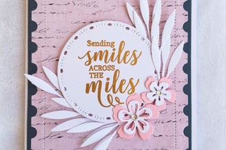 Greeting card with the message "Sending smiles across the miles" in gold on a round white cutout. Pi