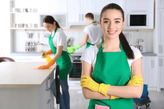 a woman in green aprons and gloves holding a cleaning sponge