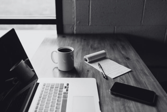 A work desk with laptop, coffee mug, notepad, pen and phone | translation services