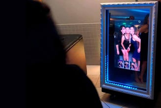 Pessoa parada em frente a um espelho mágico com a foto de uma mulher numa festa de casamento.