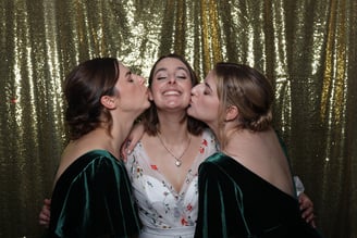 A bride is kissed by two bridesmaids at her wedding event in the get the picture vintage photo booth Brighton golden backdrop