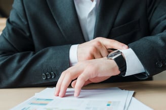 Business man looking at watch, while working in a office desktop.