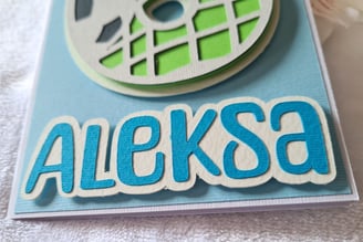 Close-up of a card featuring the name "Aleksa" in bold blue letters on a white background