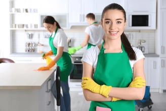 a woman in green aprons and gloves holding a cleaning sponge
